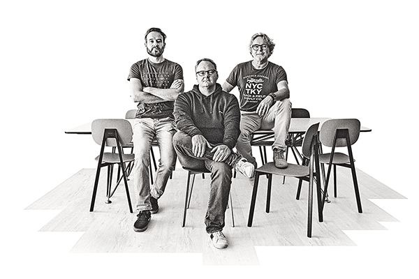 Drei Männer aus dem Partner in Crime Team sitzen und stehen vor einem Tisch. Matthias Lehner, Heiko Hinkofer und Dida Zollner