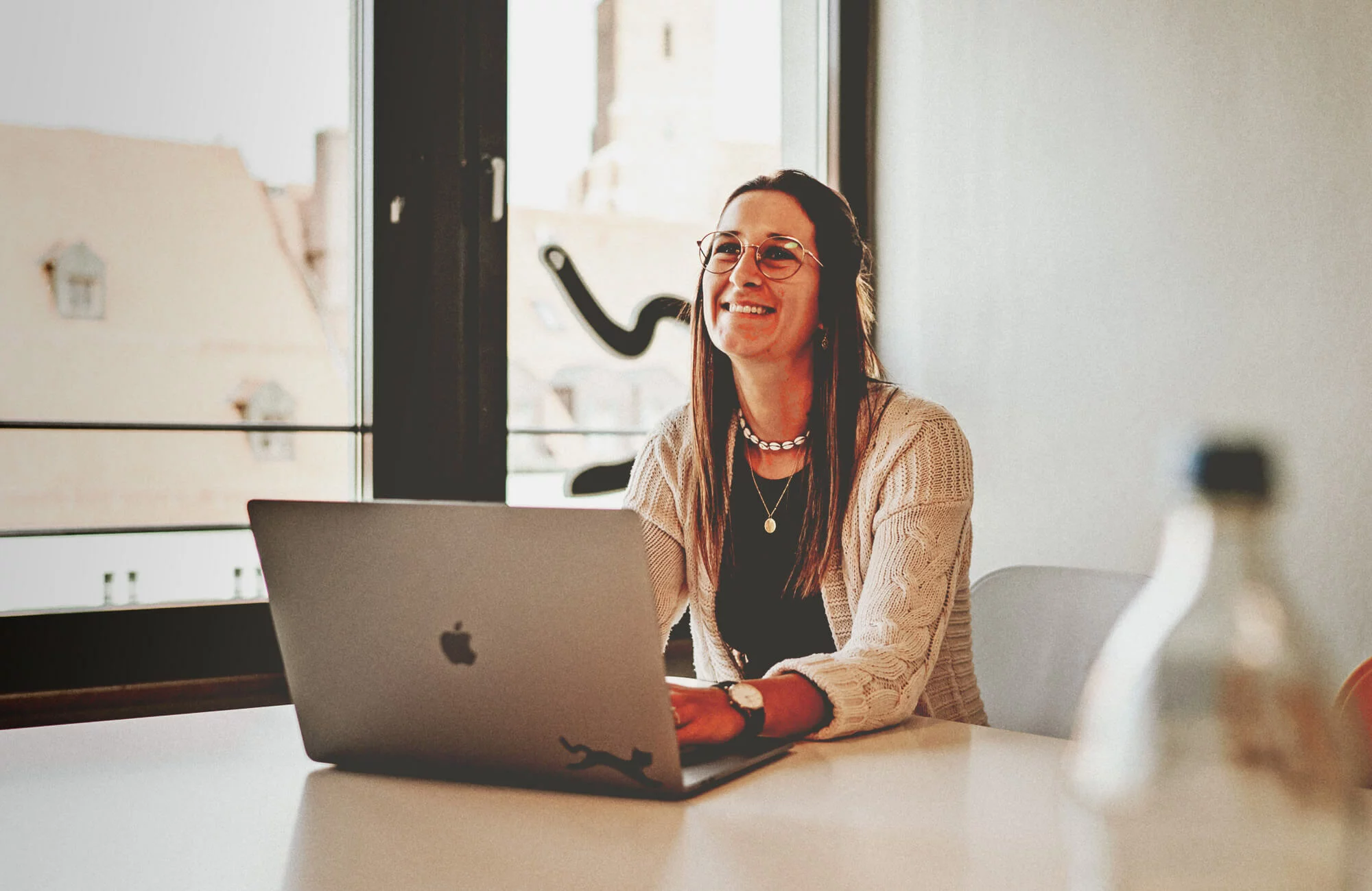 Frau sitzt mit Laptop am Tisch und lächelt.
